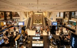 A bustling scene inside a modern shopping mall with escalators and various retail stalls.